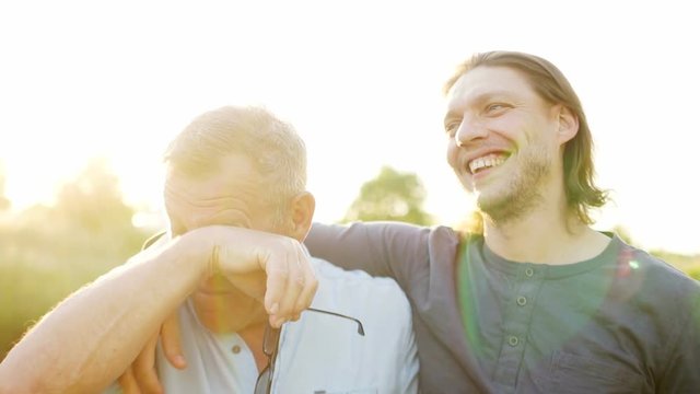 Father and son have a good time on the river bank. Evening sunset. The men talk and laugh. Father takes off his glasses and rubs his eyes. Fathers day