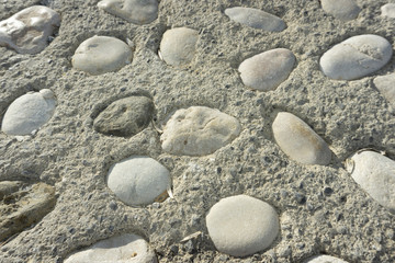 Fototapeta na wymiar Texturas de yeso y muro color gris rugoso con piedras ovaladas incrustadas