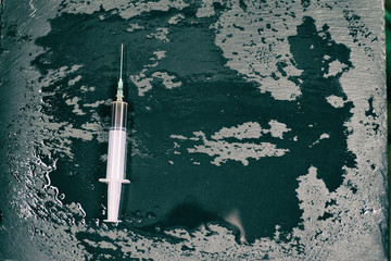 Syringe with a dark liquid on a dark wet background.