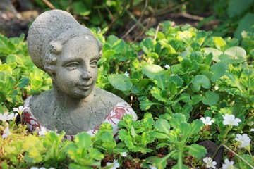 Obraz premium Grey concrete garden decor bust of woman between green plant in garden