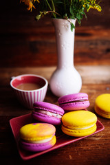 colored macaroons, coffee Cup and flower bouquet on wooden brown background,