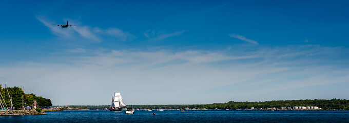 Tall Ship in full sail on the St. Lawrence River with a military transport airplane flyover