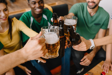 closeup view of multicultural football fans celebrating and clinking beer bottles and glasses