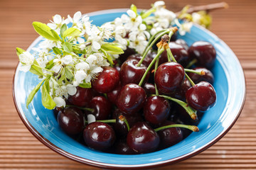 fresh cherries in a blue bowl with wild flowers On a wooden windowsill