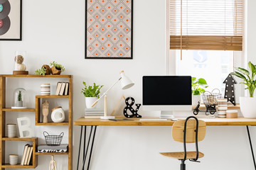 Real photo of a desk with a computer screen, lamp and ornaments standing with a chair next to a...