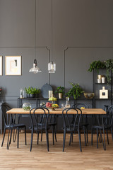 Black chairs at wooden table in grey dining room interior with lamps and plants. Real photo