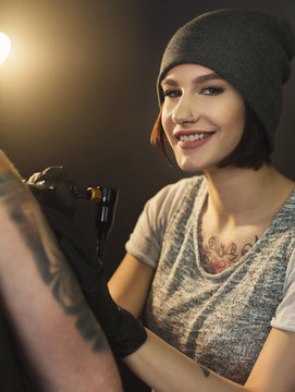 Young woman tattooist doing tattoo on shoulder