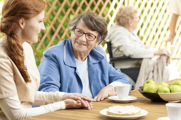 Happy grandmother drinking tea while caregiver taking care of her