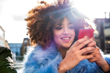 Portrait of woman with afro looking at smartphone smiling