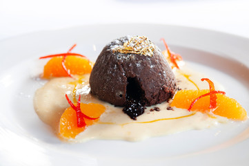 French dessert. Chocolate fondant lava cake with vanilla sauce, citrus and gold leaf on white plate...