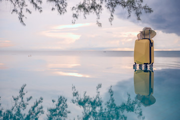 Fototapeta na wymiar Traveling suitcase and hat on Beautiful seascape with shadow of trees, swimming pool, sea and reflection, traveling and relaxing time concept.