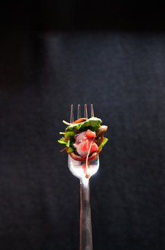Fresh octopus carpacio with spinach salad pesto balsamic dressing on silver fork, isolated on dark background