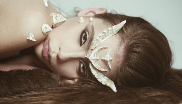 Fairy tale creature with thorns on skin lying on black fur rug. Female devil with cunning look tempting people. Girl with artistic make-up isolated on white background., fantasy concept