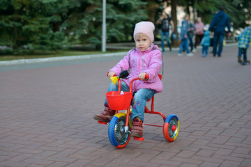little girl in a jacket is riding in a park on a tricycle