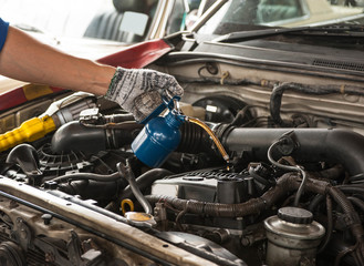 Asian mechanic is using the engine oil to repair the engine at garage