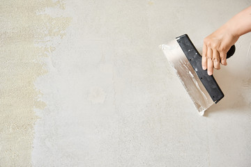 Spatula with putty in hand. Worker puts of plaster on wall.
