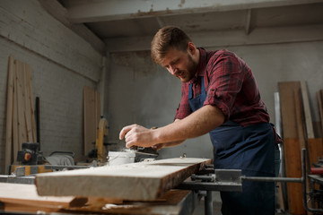 Master carpenter in shirt and apron strokes  plane in workshop