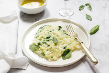 Gentle cream risotto with spinach, served with wine. Light background.