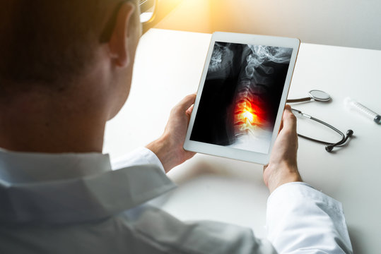 Doctor holding a digital tablet with x-ray about spine with pain in the neck. Stethoscope on the desk