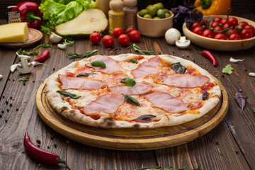 Delicious italian pizza with ham and basil leaves on wooden background