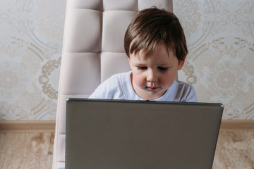 the boy is sitting on a chair and is holding a laptop