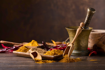 Various Indian spices with wooden spoons on a wooden table.