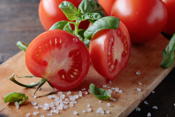 Red tomatoes with green basil on wooden table.