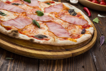 Delicious italian pizza with ham and basil leaves on wooden background