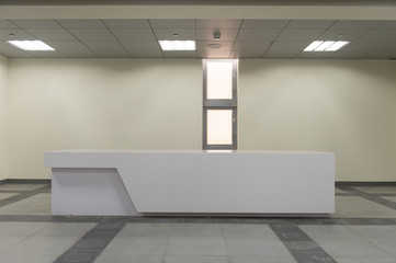 Reception desk in a corridor with large panoramic window with wide shades and rectangular pattern.