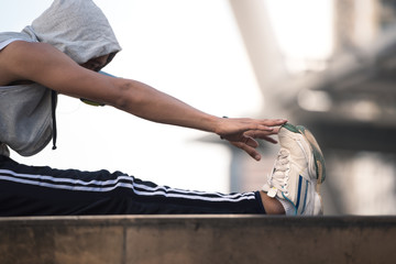 Young man stretching his body muscles , arms, legs, neck before running on the cityscape background.