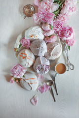 Beautiful pink, rose peonies decorated with tasty meringues on white wood table, with vintage...