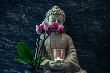 Buddha statue with candle in hands and pink orchid flower ahead