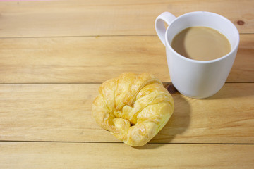 Croissant and coffee on wooden table.