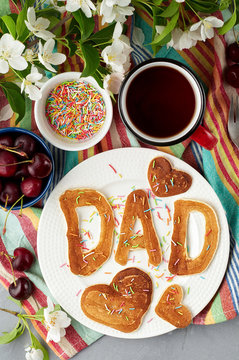 Special Father's Day breakfast. Alphabet Pancakes with sprinkles, cherries and cup of tea on a gray concrete background