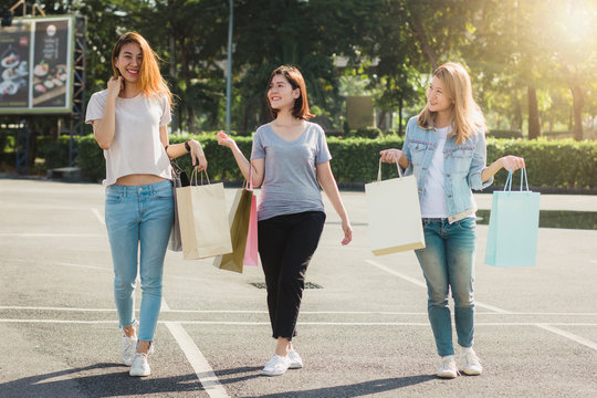 Group of young Asian Woman shopping in an outdoor market with shopping bags in their hands. Young women show what they got in shopping bag under warm sunlight. Group outdoor shopping concept.