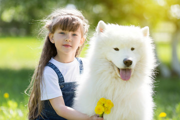 Little girl with a big white dog in the park. A beautiful 5 year old girl in jeans hugs her favorite dog during a summer walk.