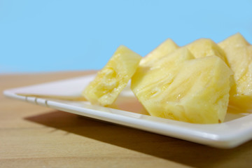 A slice of pineapple on wooden table in cyan background closeup. 