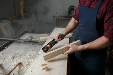 Master carpenter in shirt and apron strokes  plane in workshop. Close up