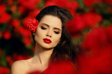 Outdoors portrait of Natural Beauty woman in red roses. Sensual female with rose flowers in hair. Sexy brunette with makeup over sunset blossom park. Passion and expression. Spanish flamenco style.
