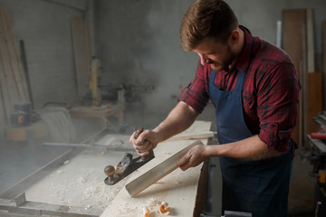 Master carpenter in shirt and apron strokes  plane in workshop. Close up