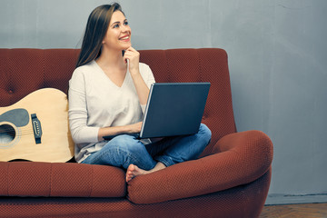 Casual dressed woman sitting on sofa with laptop.