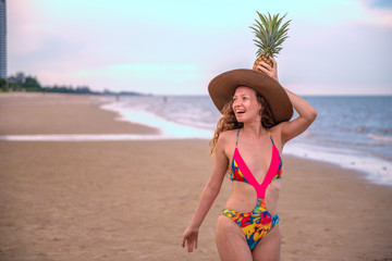 Portrait happy woman with long blonde curly hair holding pineapple on the beach with enjoying and refreshing, summer beach relaxing time concept.