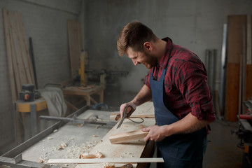 Master carpenter in  shirt and apron works as an ax in workshop
