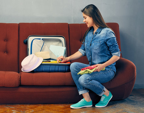 Smiling woman sitting on couch with clothes in suitcase.