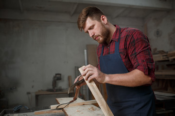 Master carpenter in  shirt and apron works as an ax in workshop