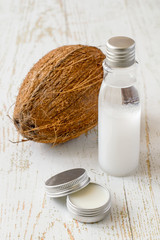Obraz na płótnie Canvas A small round jar and a plastic bottle with natural coconut oil, next to a fresh coconut on an old wooden table. Used in cosmetology for skin care of face and body.