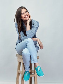 Smiling young woman sitting on stool with crossed legs.