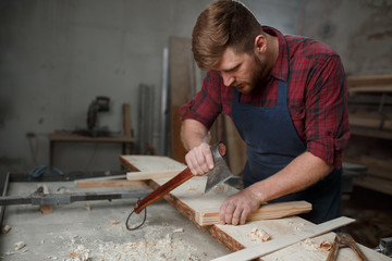Master carpenter in  shirt and apron works as an ax in workshop