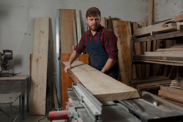 Naklejka na ściany i meble Master carpenter saws the board on machine in workshop