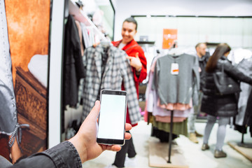 man looking into phone while his girlfriend do shopping in boutique